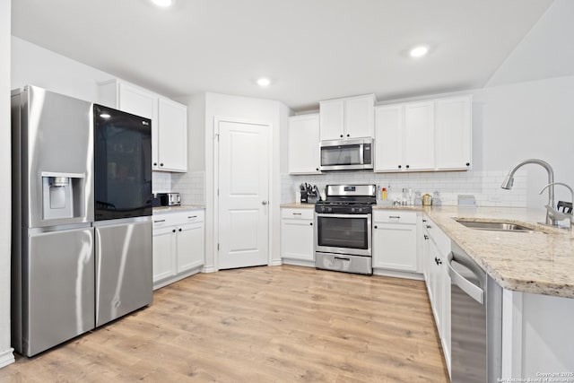 kitchen with stainless steel appliances, a sink, white cabinets, light wood-style floors, and light stone countertops