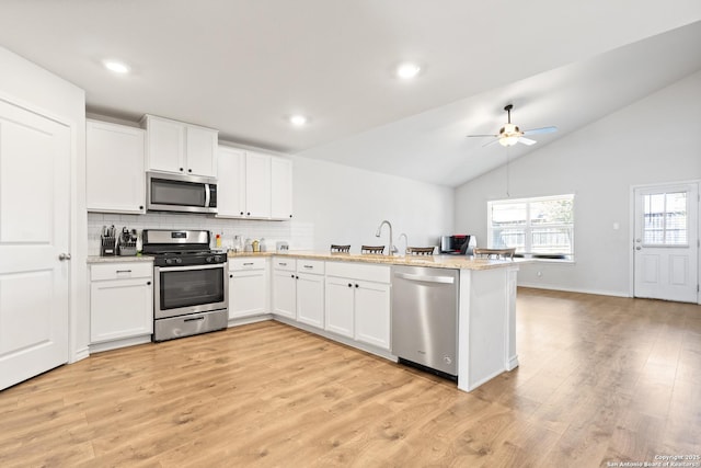 kitchen with a peninsula, white cabinetry, appliances with stainless steel finishes, decorative backsplash, and light wood finished floors