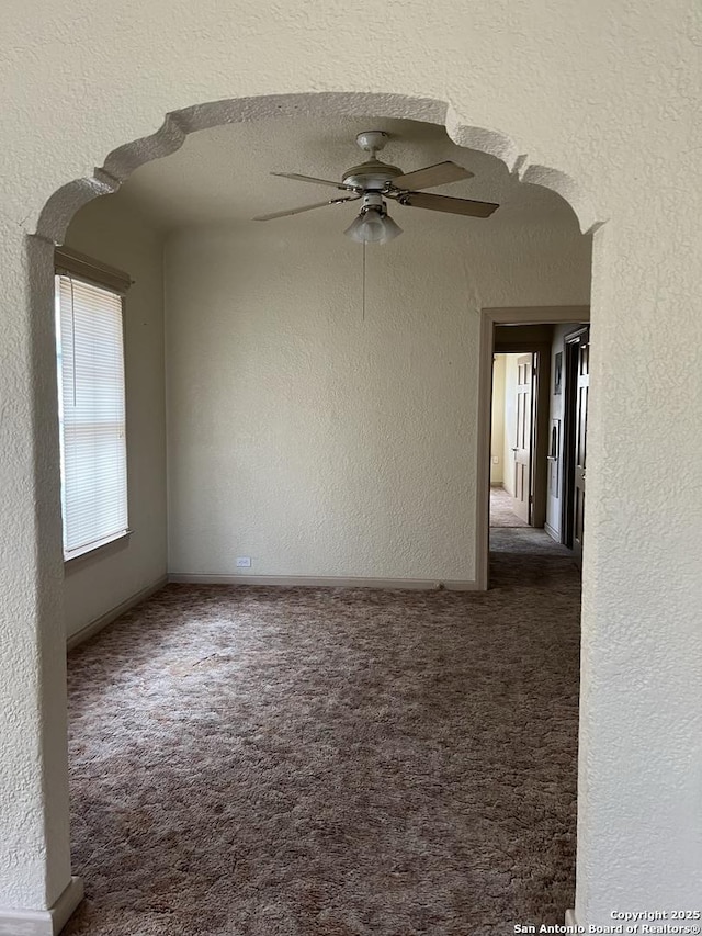 carpeted empty room featuring arched walkways, a textured wall, a textured ceiling, and ceiling fan