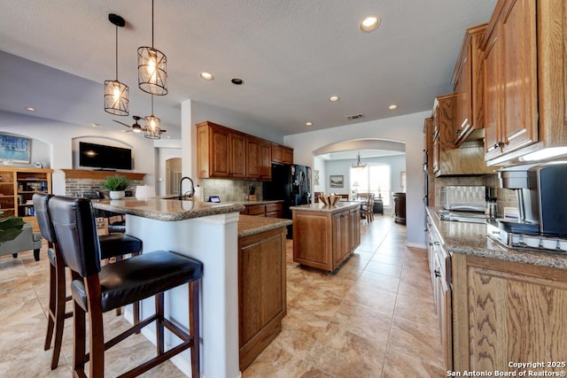 kitchen with arched walkways, a center island, brown cabinets, visible vents, and decorative backsplash