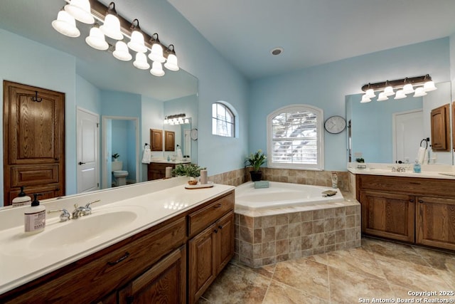 full bathroom with two vanities, a garden tub, a sink, and toilet