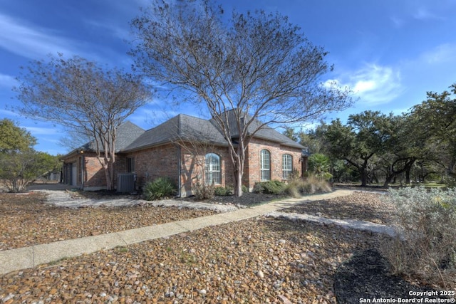 view of front of home with brick siding, an attached garage, and central air condition unit