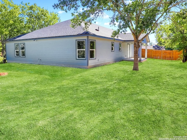 rear view of property with a shingled roof, fence, and a yard