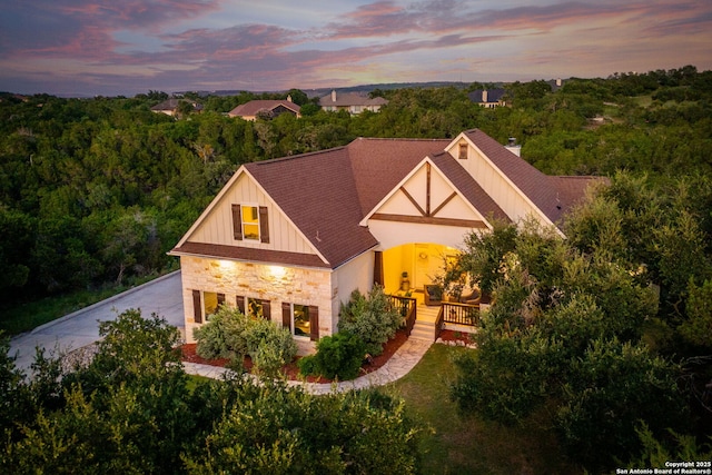 view of front of property featuring a shingled roof, stone siding, driveway, board and batten siding, and a chimney