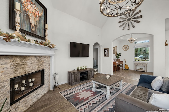 living area with arched walkways, high vaulted ceiling, a stone fireplace, a notable chandelier, and wood finished floors