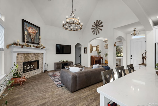 living area featuring a fireplace, high vaulted ceiling, a notable chandelier, and wood finished floors