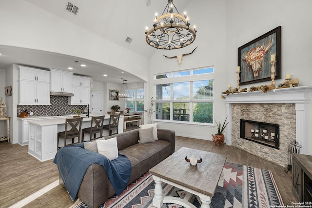 living room with light wood-type flooring, visible vents, a stone fireplace, and an inviting chandelier