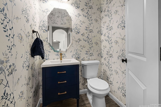 bathroom with toilet, vanity, wood finished floors, baseboards, and wallpapered walls