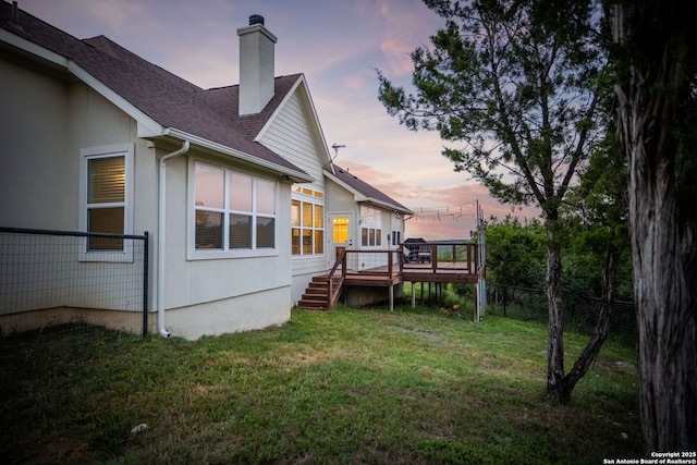 exterior space featuring a shingled roof, a lawn, a chimney, fence, and a deck