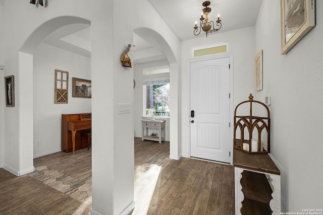 entrance foyer featuring arched walkways, baseboards, an inviting chandelier, and wood finished floors