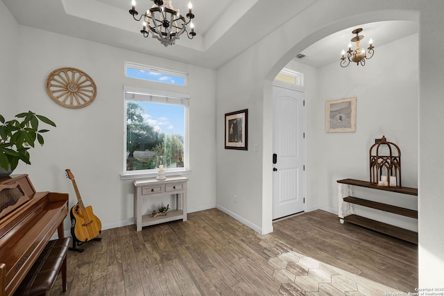 entryway featuring a chandelier, a raised ceiling, arched walkways, and wood finished floors