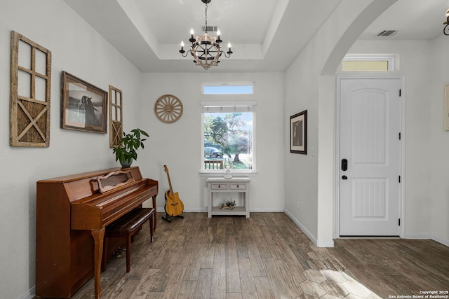 foyer featuring arched walkways, wood finished floors, visible vents, baseboards, and a raised ceiling