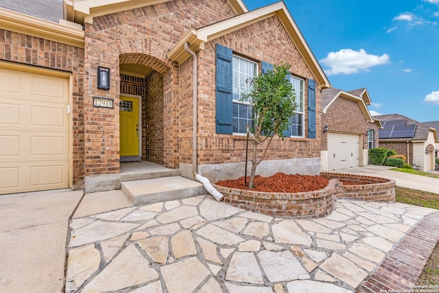 doorway to property featuring an attached garage, driveway, and brick siding