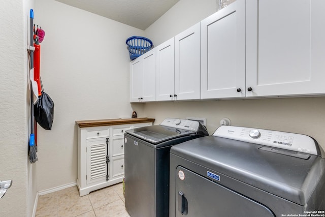 washroom featuring light tile patterned floors, separate washer and dryer, cabinet space, and baseboards