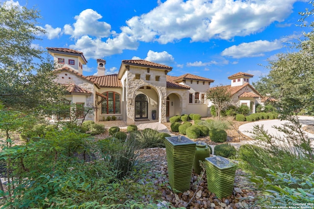 view of front of property with a tiled roof, stone siding, a chimney, and stucco siding