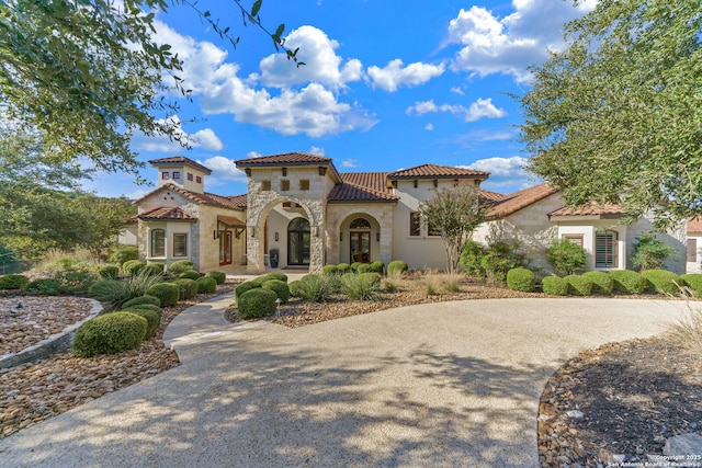 mediterranean / spanish-style house with stone siding, a tile roof, and stucco siding