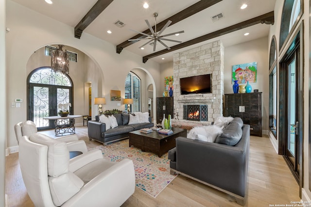 living room featuring light wood-type flooring, visible vents, a stone fireplace, and ceiling fan with notable chandelier