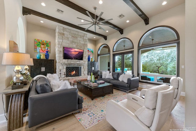 living room featuring light wood-type flooring, a fireplace, visible vents, and beam ceiling