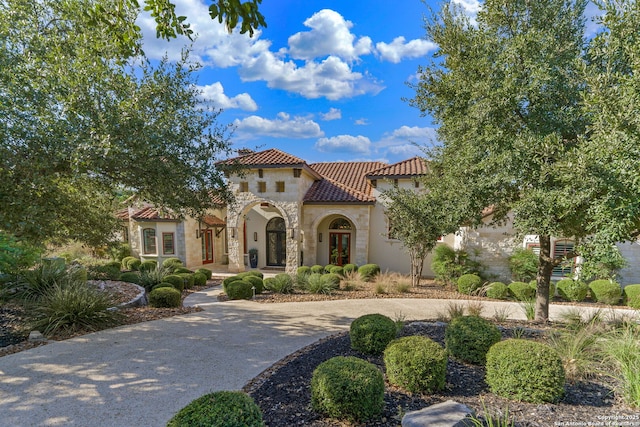 mediterranean / spanish home with stone siding, a tiled roof, and stucco siding