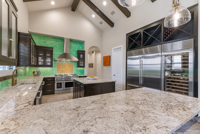 kitchen with premium appliances, arched walkways, decorative backsplash, a sink, and wall chimney range hood