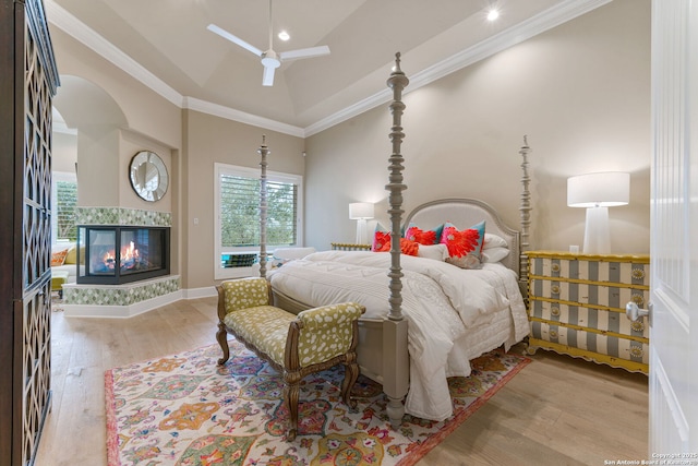 bedroom with ceiling fan, wood finished floors, a multi sided fireplace, vaulted ceiling, and ornamental molding