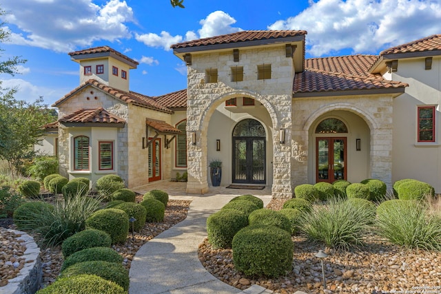 mediterranean / spanish-style home with stucco siding, a tile roof, stone siding, and french doors