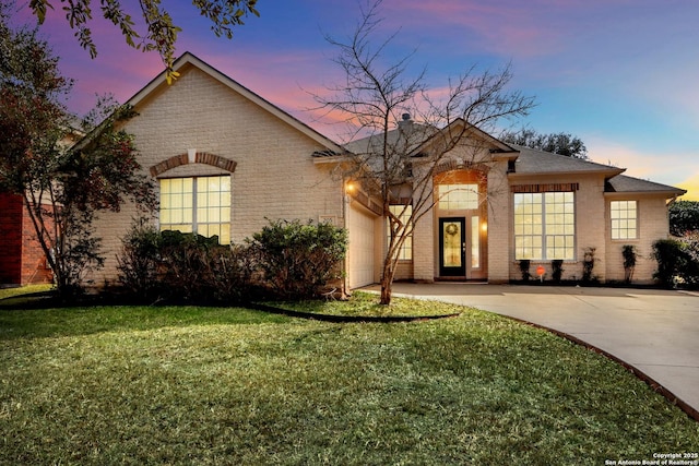 view of front facade featuring a garage, a yard, driveway, and brick siding