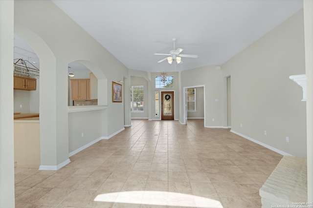 unfurnished living room featuring ceiling fan with notable chandelier, light tile patterned floors, arched walkways, and baseboards