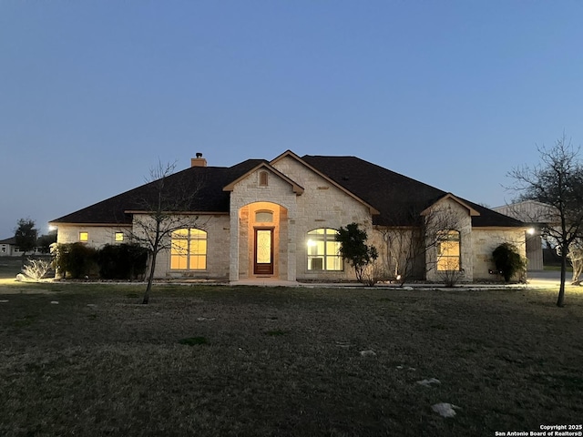 french country style house with stone siding, a chimney, and a front yard