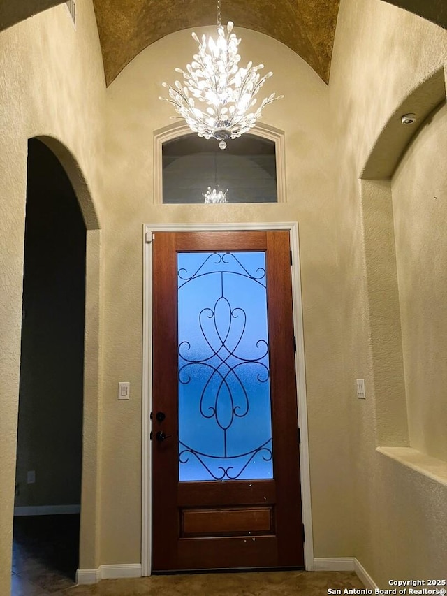 entryway with a chandelier, baseboards, and vaulted ceiling