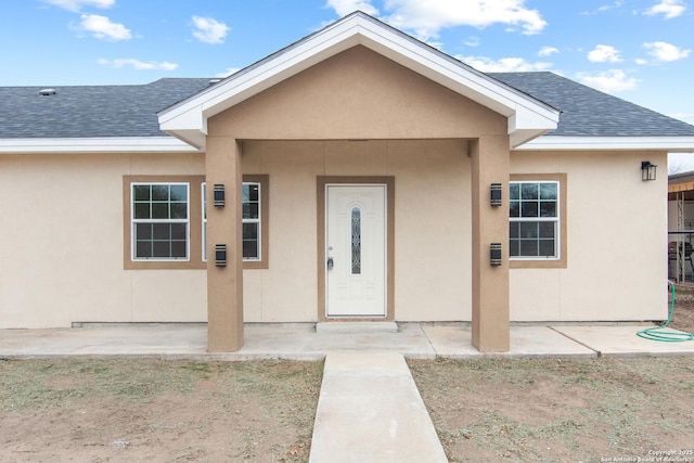 view of exterior entry featuring roof with shingles, a patio, and stucco siding