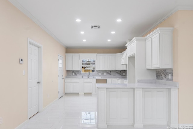 kitchen featuring visible vents, ornamental molding, a peninsula, light countertops, and white cabinetry