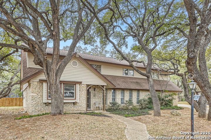 traditional home featuring a shingled roof, stone siding, and fence