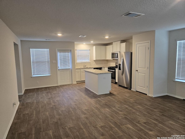 kitchen with appliances with stainless steel finishes, dark wood-style flooring, visible vents, and a center island