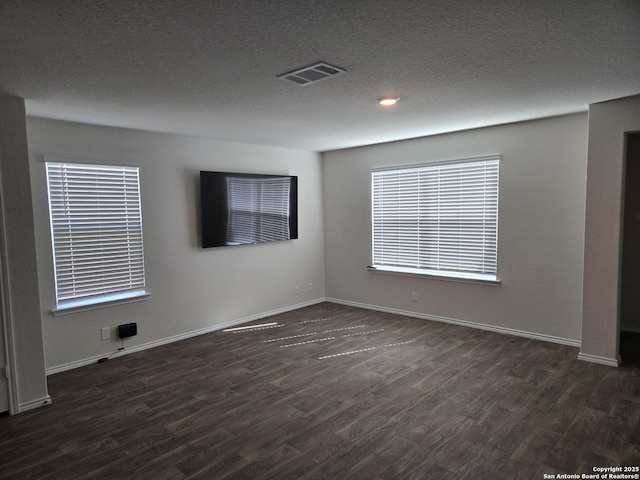 spare room with dark wood-type flooring, visible vents, a textured ceiling, and baseboards