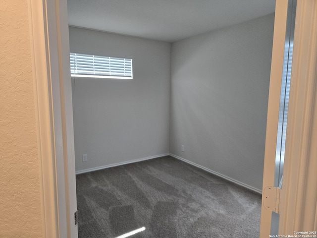 spare room with baseboards and dark colored carpet