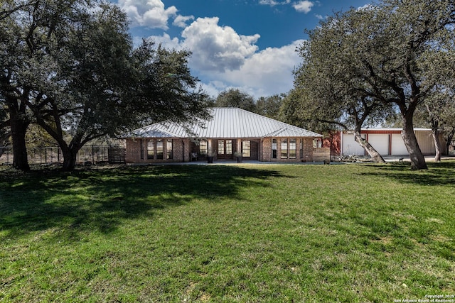 rear view of house featuring metal roof, brick siding, a lawn, and fence