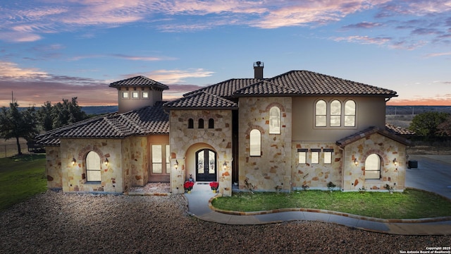 mediterranean / spanish house with stone siding, french doors, a tiled roof, and stucco siding