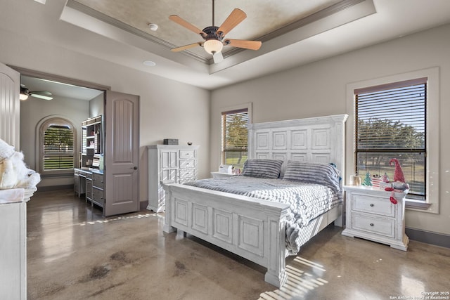 bedroom featuring finished concrete flooring, baseboards, ceiling fan, ornamental molding, and a tray ceiling