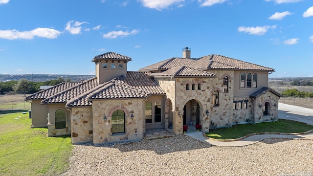 mediterranean / spanish home featuring stone siding, a tile roof, a chimney, and a front lawn