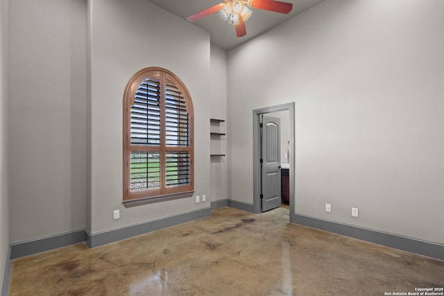 spare room with a towering ceiling, a ceiling fan, and baseboards