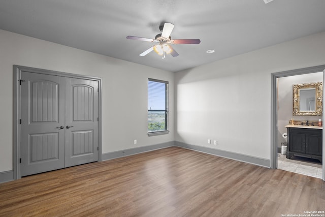 unfurnished bedroom featuring ceiling fan, a sink, baseboards, a closet, and light wood finished floors