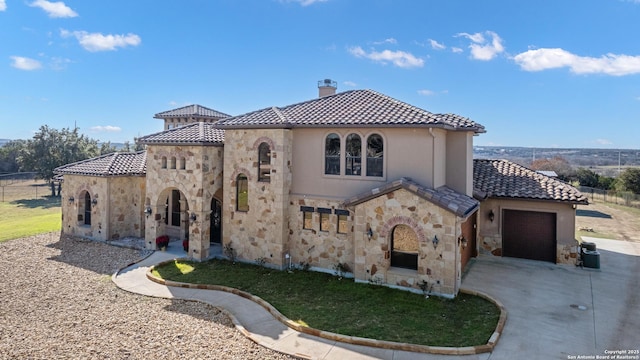 mediterranean / spanish house with an attached garage, stone siding, a chimney, and a tiled roof