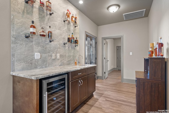 bar featuring beverage cooler, a sink, visible vents, light wood-style floors, and wet bar