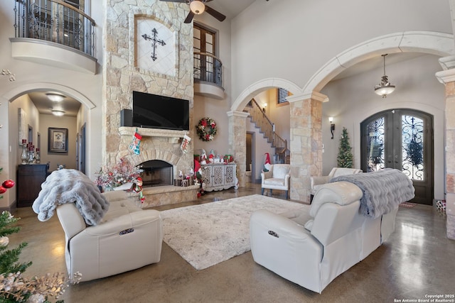 living area with a towering ceiling, arched walkways, french doors, and a stone fireplace