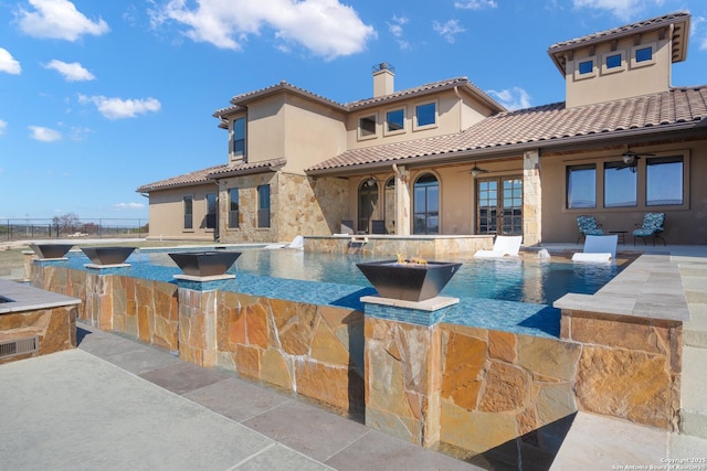 back of house with a patio area, stone siding, ceiling fan, and a chimney