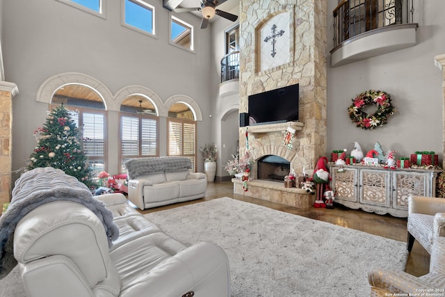 living area featuring ceiling fan, plenty of natural light, a stone fireplace, and wood finished floors