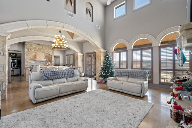 living area featuring an inviting chandelier, visible vents, arched walkways, and ornate columns