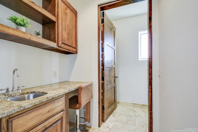 kitchen with light stone countertops, open shelves, a sink, and brown cabinetry