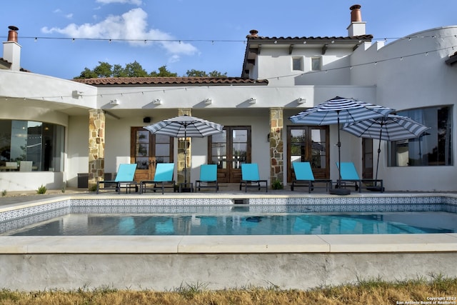 back of property with an outdoor pool, french doors, a patio area, and stucco siding